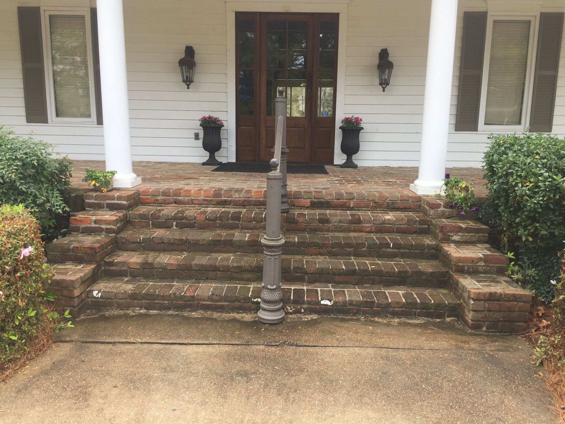 Brick steps leading up to the front door of a white house with large columns and two flower pots.