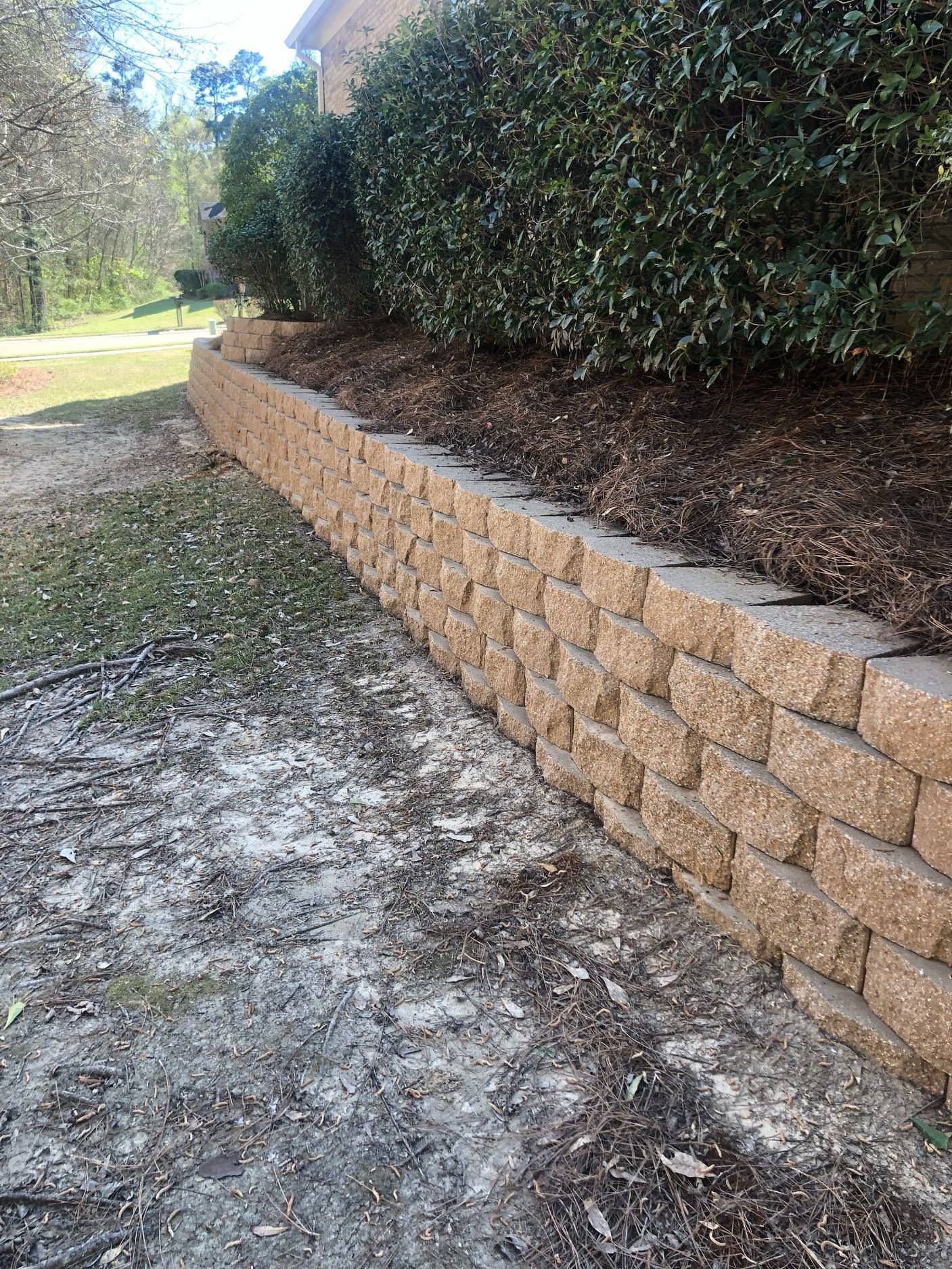 Tan block retaining wall bordering mulch and greenery.