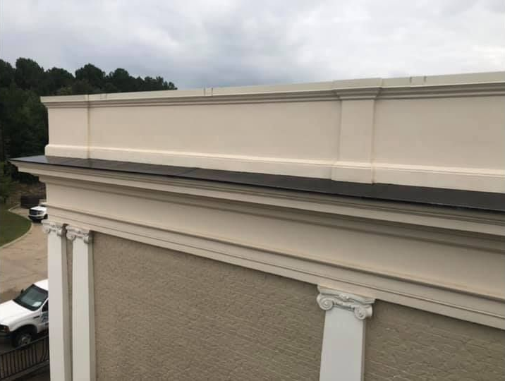 Building exterior detail, showing cream-colored trim and brick, with a dark roof and overcast sky.