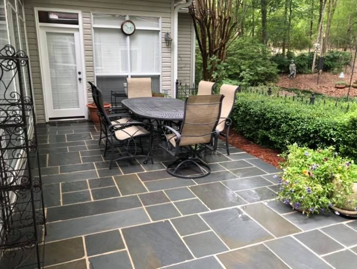 Patio with dark stone tiles, table with chairs, and lush greenery.
