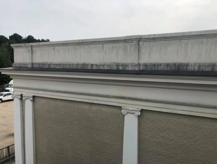Exterior building detail with ornate trim, weathered concrete, and a cloudy sky.