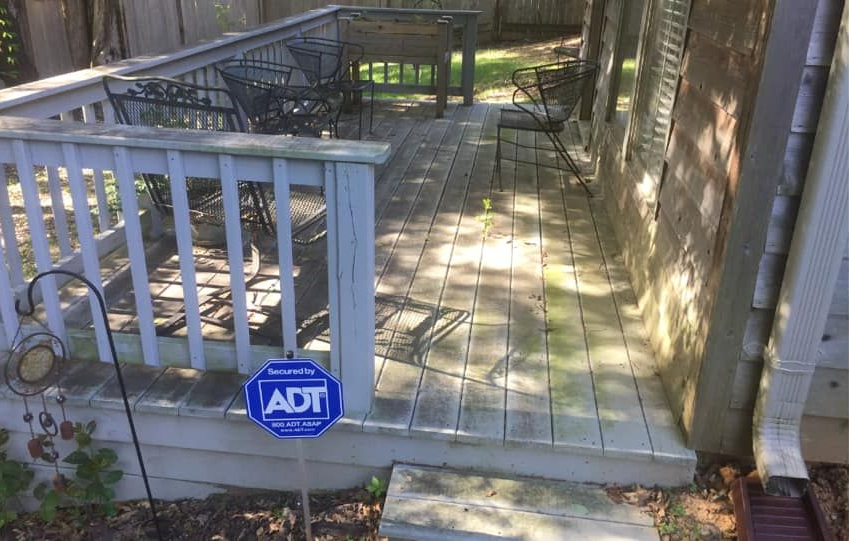 Wooden deck with weathered planks and railing.  Outdoor seating and an ADT security sign are present.