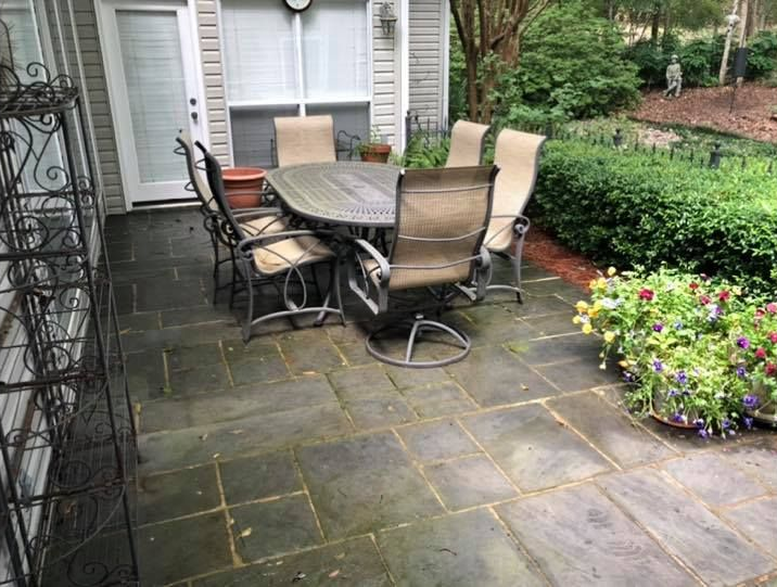 Patio with stone pavers, outdoor dining set, and surrounding greenery.