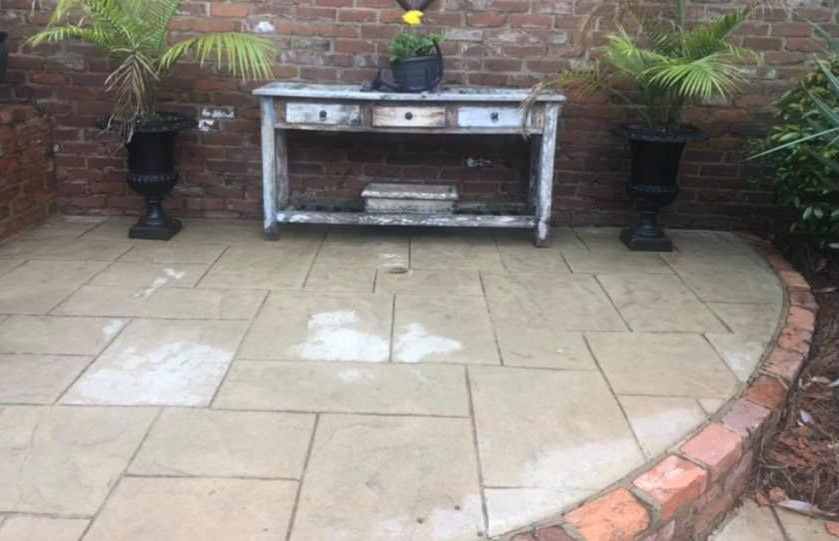Patio with brick wall and raised edge, stone pavers, weathered table, potted plants, and urns.
