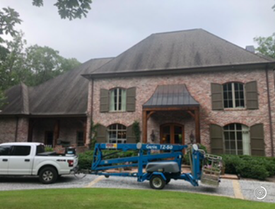 A large brick house with a white truck and blue lift in the yard, likely for roof cleaning.