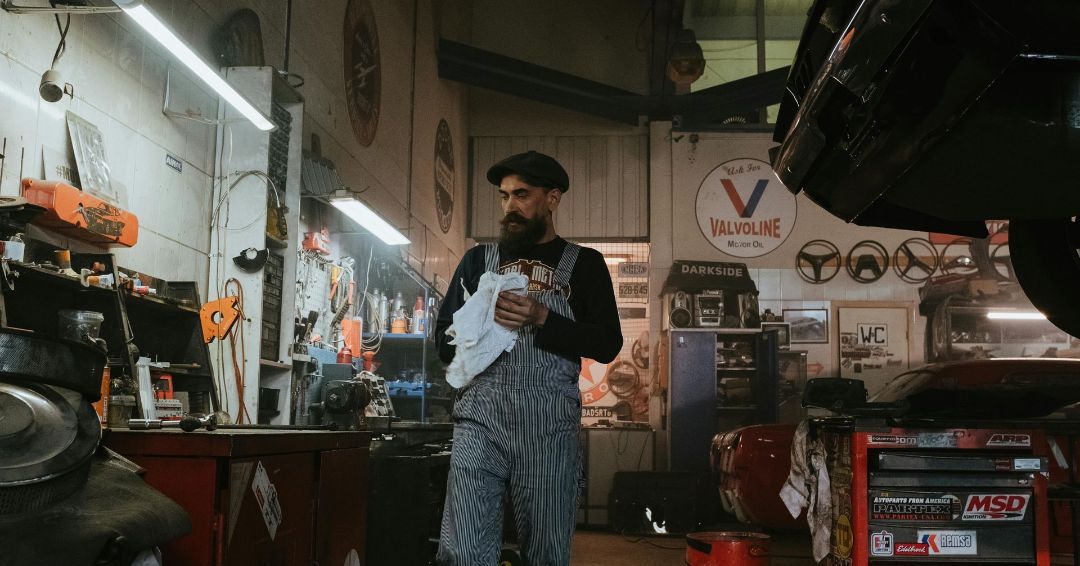 A man in overalls is standing in a garage holding a piece of paper.