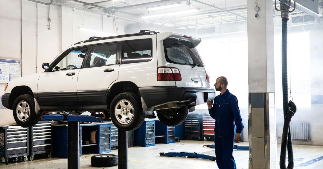 A man is standing next to a car on a lift in a garage.