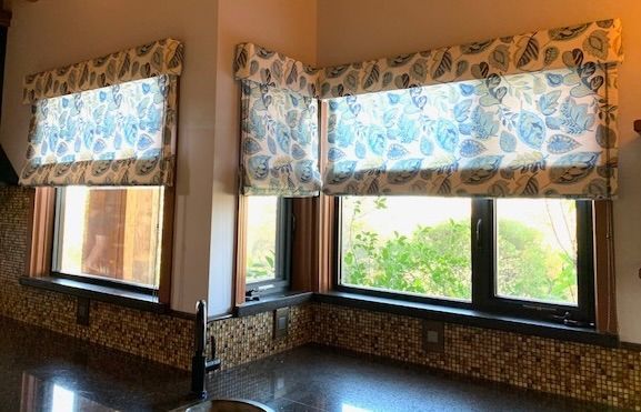 A Kitchen with A Sink and Two Windows with Roman Shades.