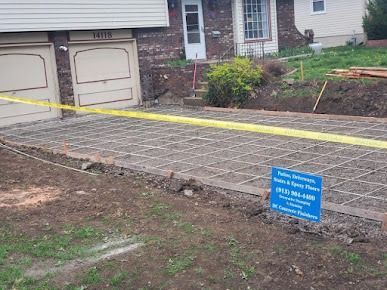 Concrete driveway under construction, with mesh reinforcement and a sign. Yellow caution tape in front.