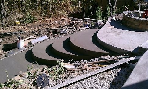 Concrete steps under construction leading to a patio with a stone fire pit.