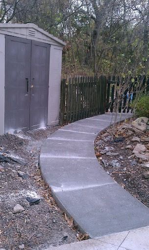 Concrete pathway curves past a shed and wooden fence.