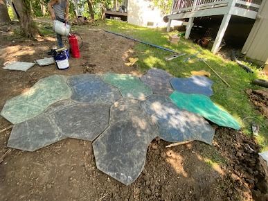 Person laying irregularly shaped paving stones in a yard near a deck and a house.