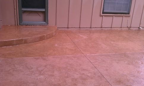 Brown-colored concrete patio with steps leading to a house with a window.