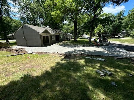Small house with newly poured concrete driveway and yard. Trees surround the property.