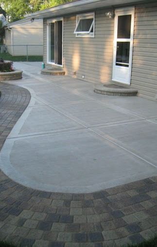 Concrete patio with brick border, next to a beige brick building with windows and a door.