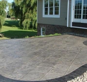Stone patio outside a house with a grass lawn and trees.