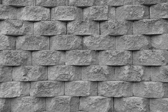 Gray, textured retaining wall made of stacked, rectangular blocks.