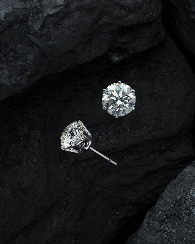 Un paio di orecchini con diamanti sono appoggiati su una superficie nera.