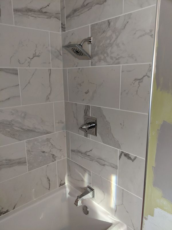 A bathroom with marble tiles, a tub, and a shower head