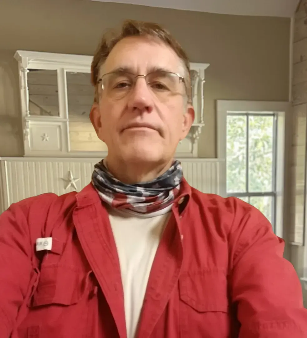 A man wearing glasses and a red shirt is taking a selfie