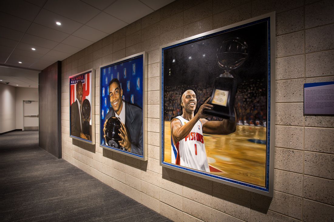 Hallway with three framed basketball portraits on brick wall.