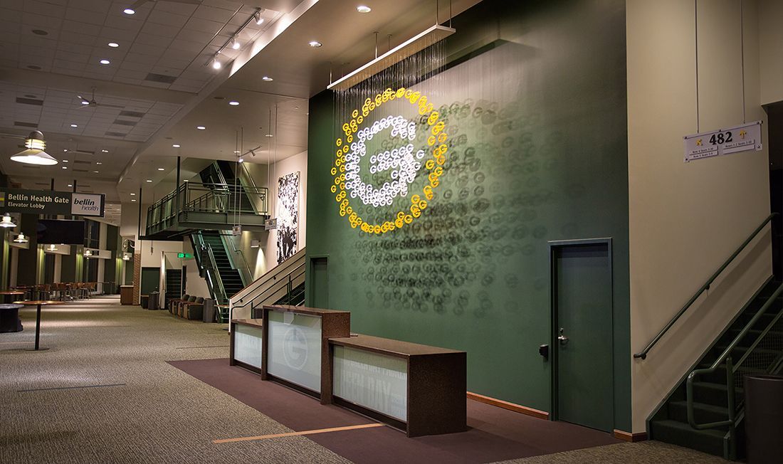 Lobby with Green Bay Packers logo on wall. Reception desk, stairs, and overhead lighting are visible.
