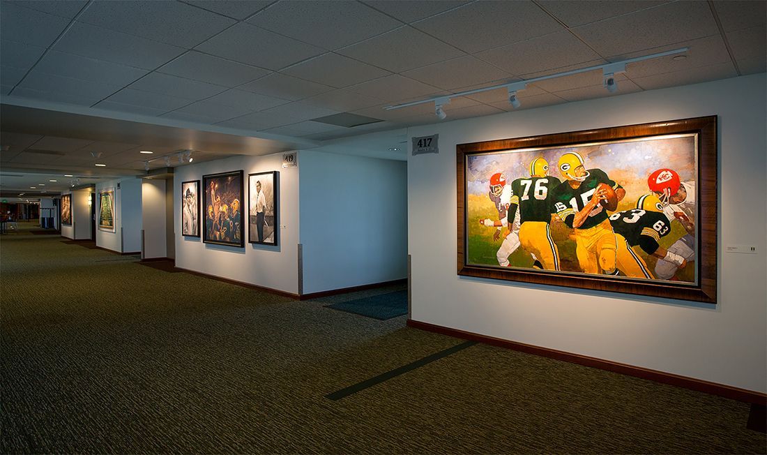Hallway with framed football art on white walls, carpeted floor.