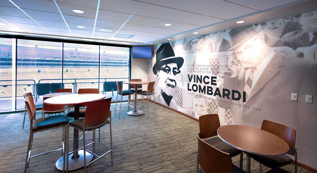 Lounge with round tables and chairs, window view, and a large mural of Vince Lombardi.