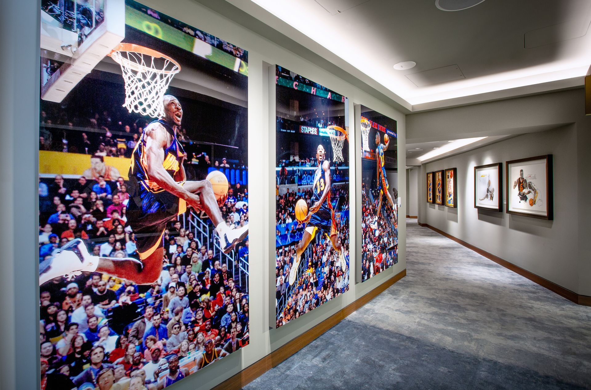 Basketball action photos line a hallway. Players dunking, with a crowd and the court visible.