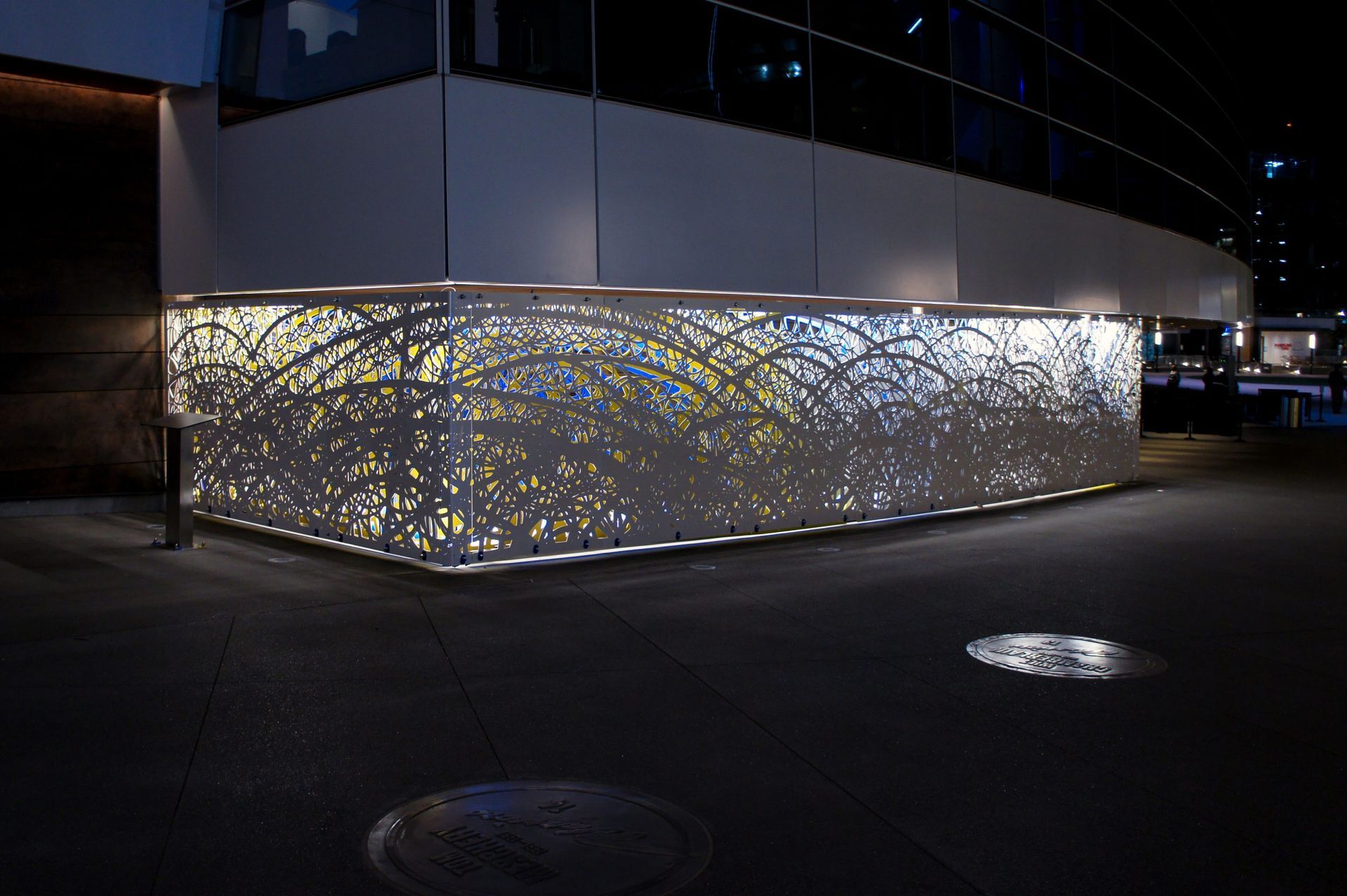 Illuminated decorative metal screen along a building exterior.