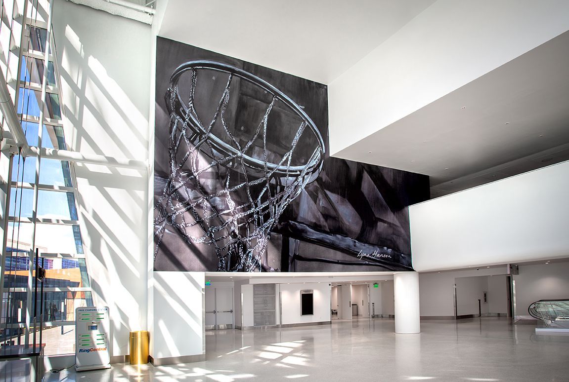 Large-scale photograph of a bicycle wheel displayed on a bright white wall in a modern lobby. Sunlight streams through a large window.
