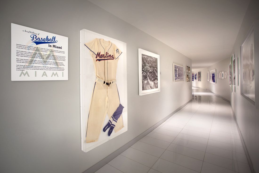 A long hallway with framed artwork on light gray walls, including a baseball jersey.
