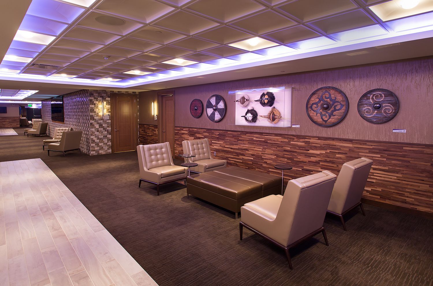 Lounge area with brick wall, seating, decorative wheels, and a square-tiled ceiling with ambient lighting.