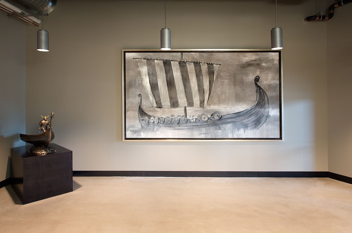 A gray-walled room with a framed artwork of a Viking ship and a sculpture on a pedestal. Three pendant lights above.