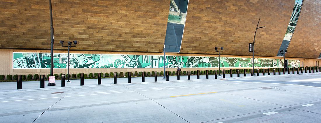 A mural on a wall beneath a bridge, with a row of bollards along the edge of the sidewalk.