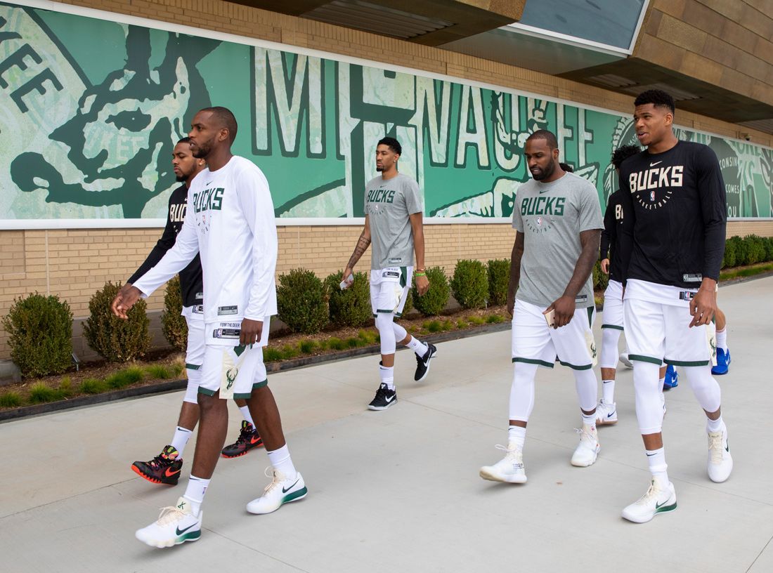 Milwaukee Bucks players walking outdoors in matching white shorts and jerseys.