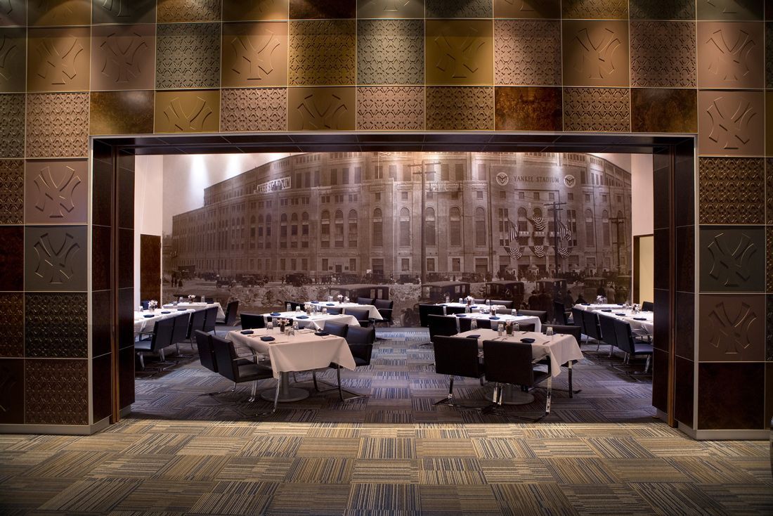 Restaurant interior: tables set for dining, building mural backdrop, patterned wall, open doorway.