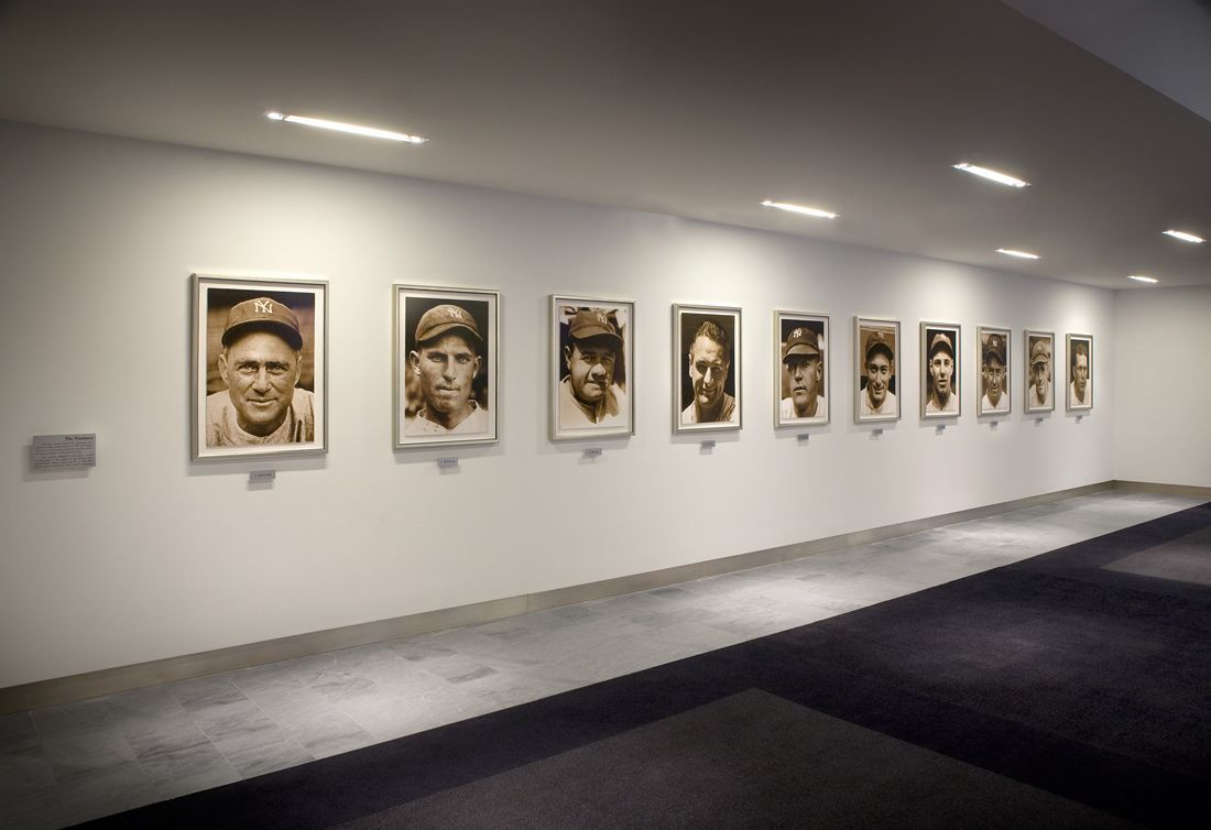 Line of framed portraits hanging on a white wall in a gallery.