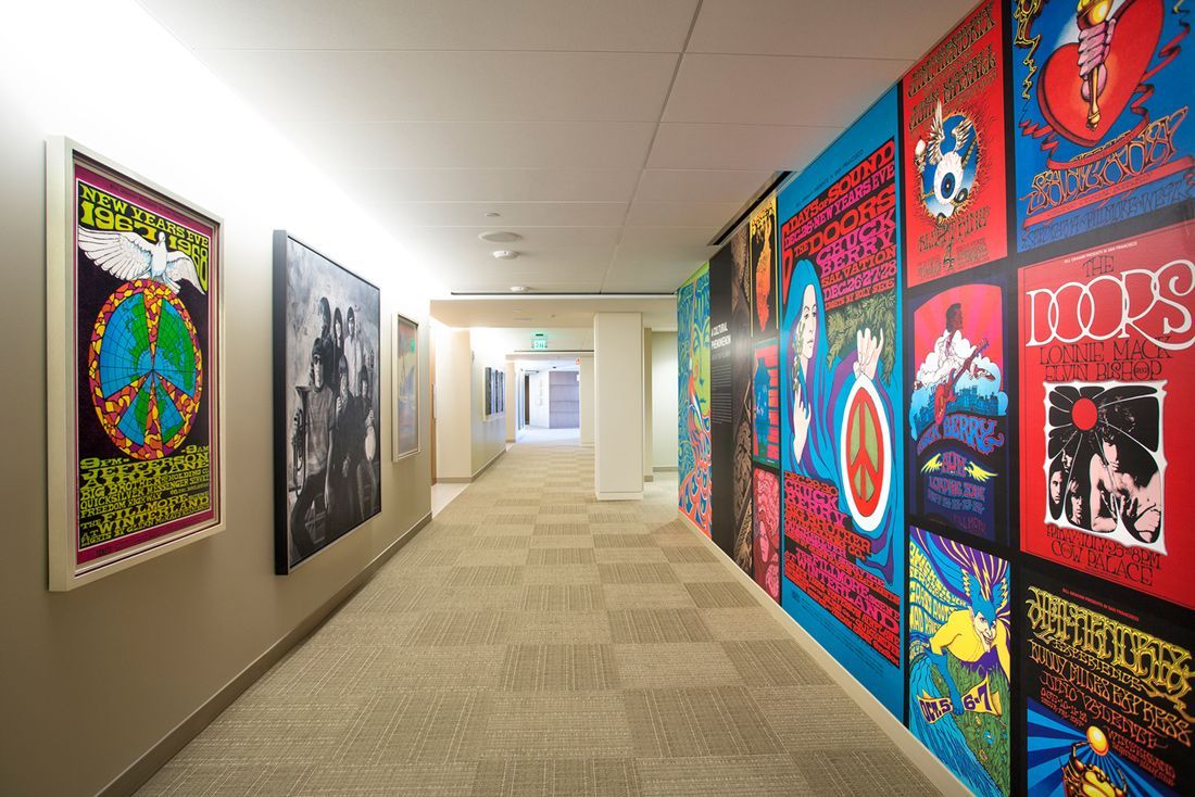 Hallway with vintage concert posters on blue wall and framed art. Beige carpet and ceiling lights.