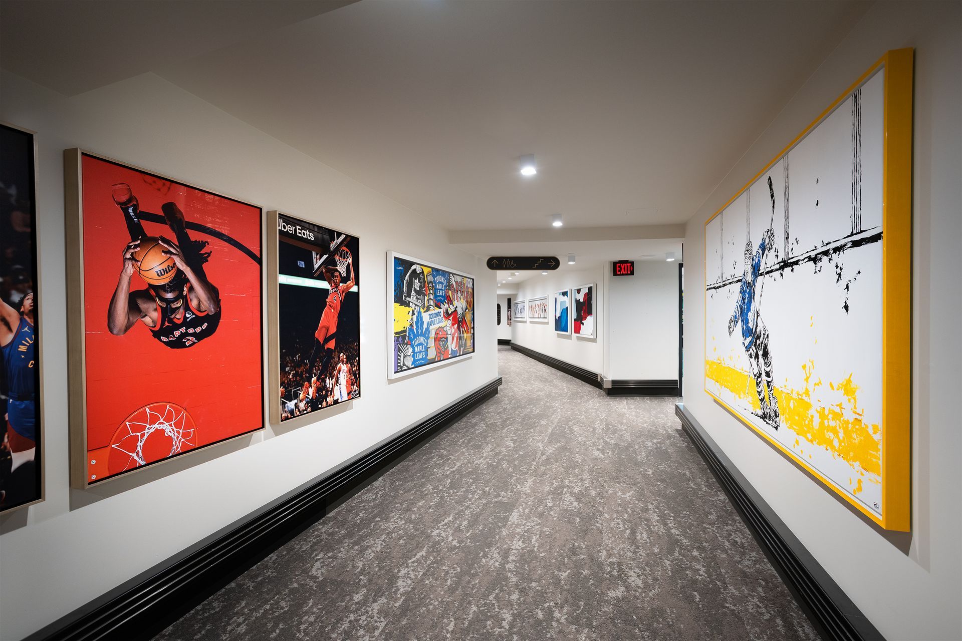 A hallway with artwork on the walls. One piece is on a red background. The floor is carpeted.