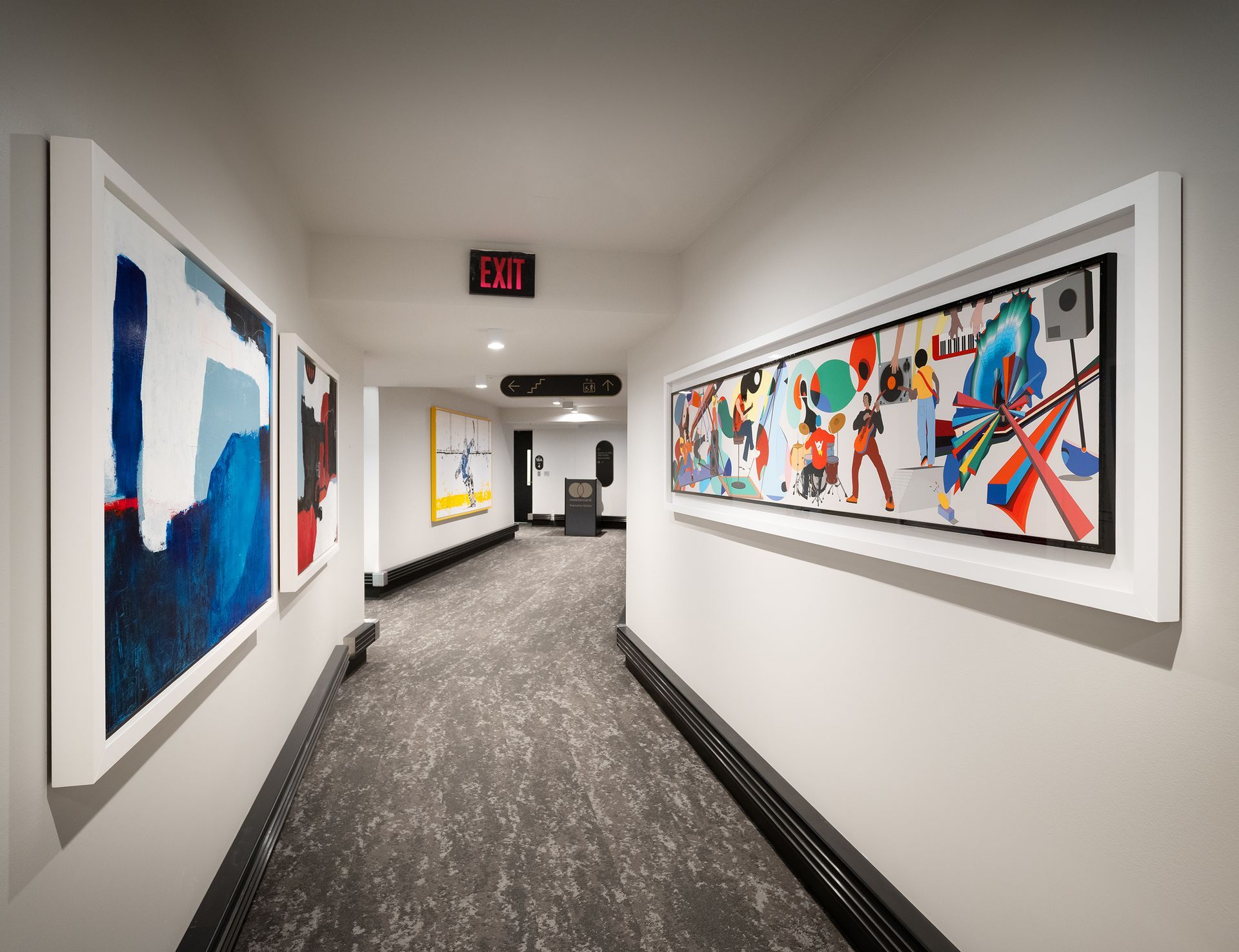 Hallway with abstract art, dark carpet, and an exit sign.