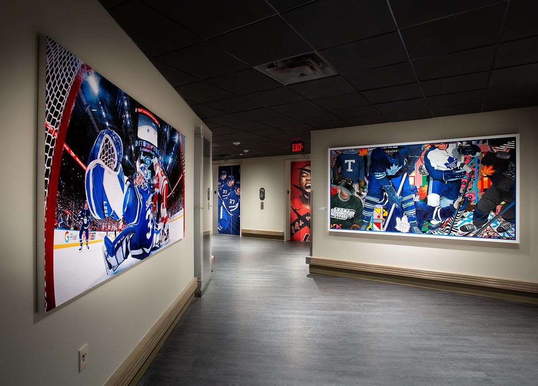 Hallway with large hockey action photos. Black ceiling, gray floor, white walls. Red exit sign.