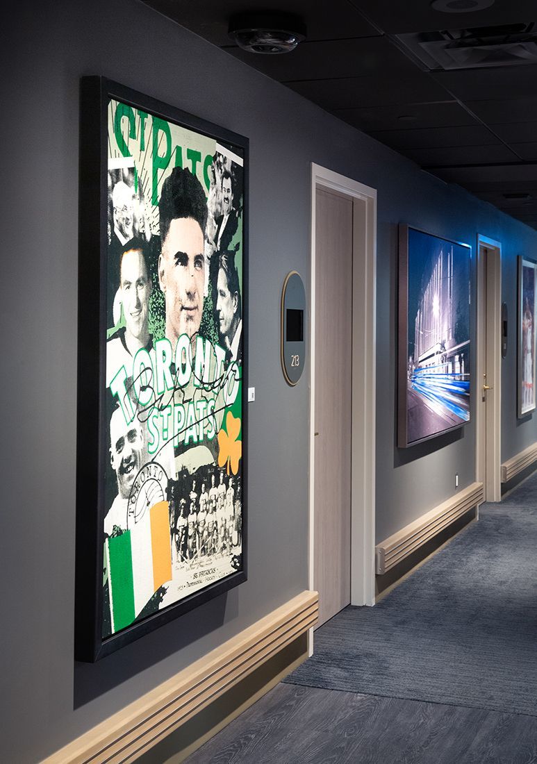 Hallway with framed art, doors, and a blue carpet. One artwork features a green, white, and orange flag.