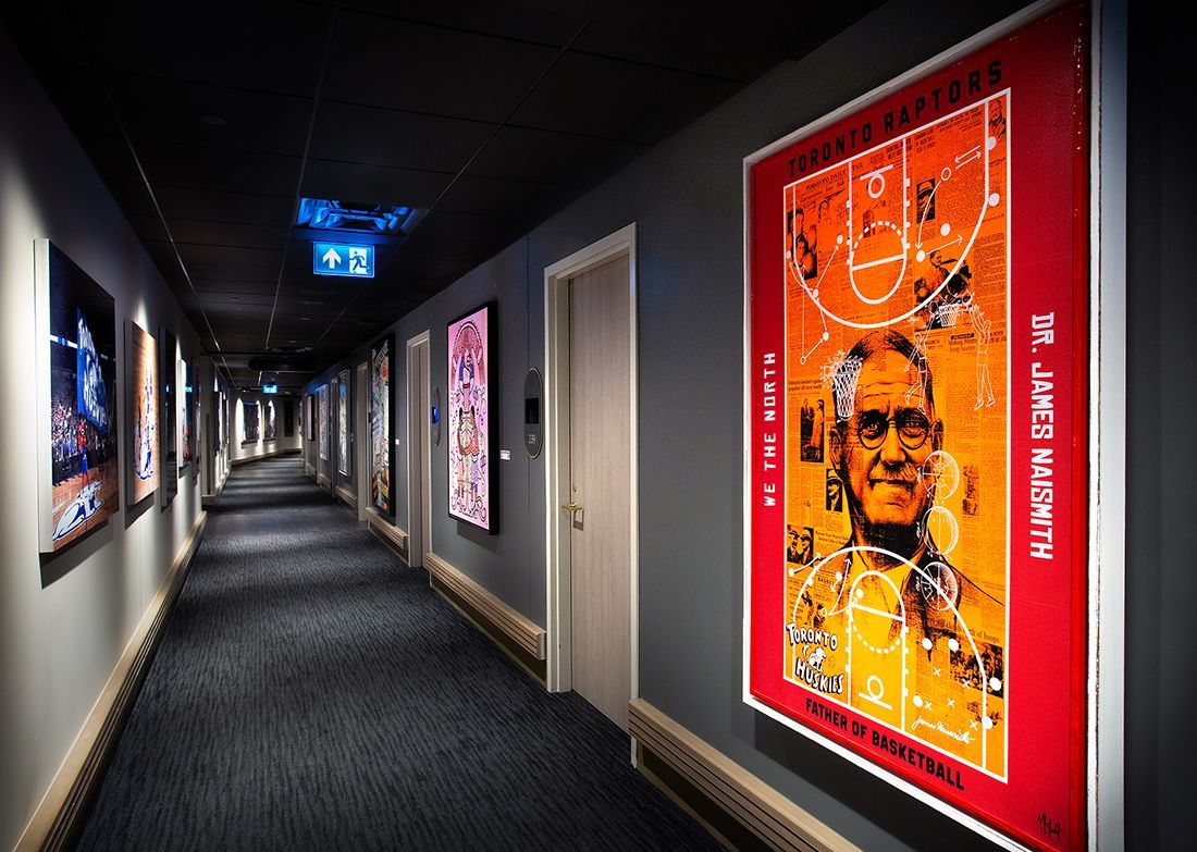Hotel hallway with art on walls; dark blue carpet, and emergency exit sign.