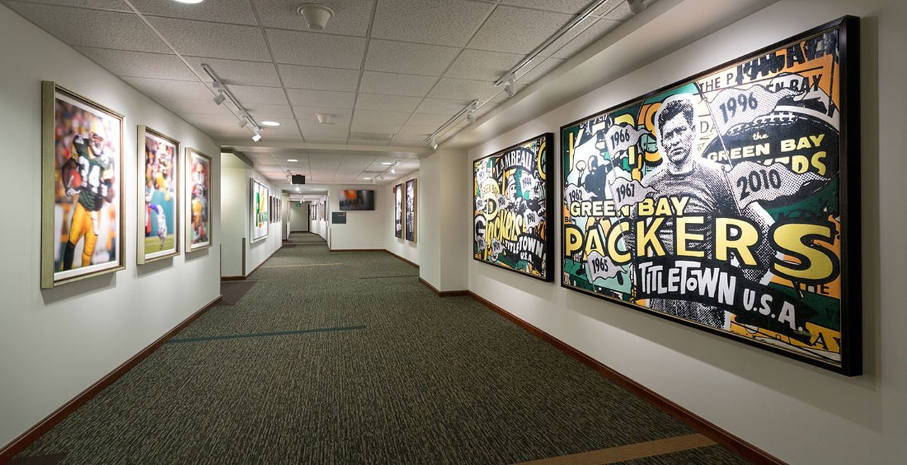 Hallway with framed sports art, primarily green and yellow, and carpet.
