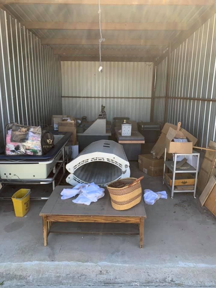 A storage unit filled with items including a tanning bed, a coffee table, a medical cart, and various boxes.