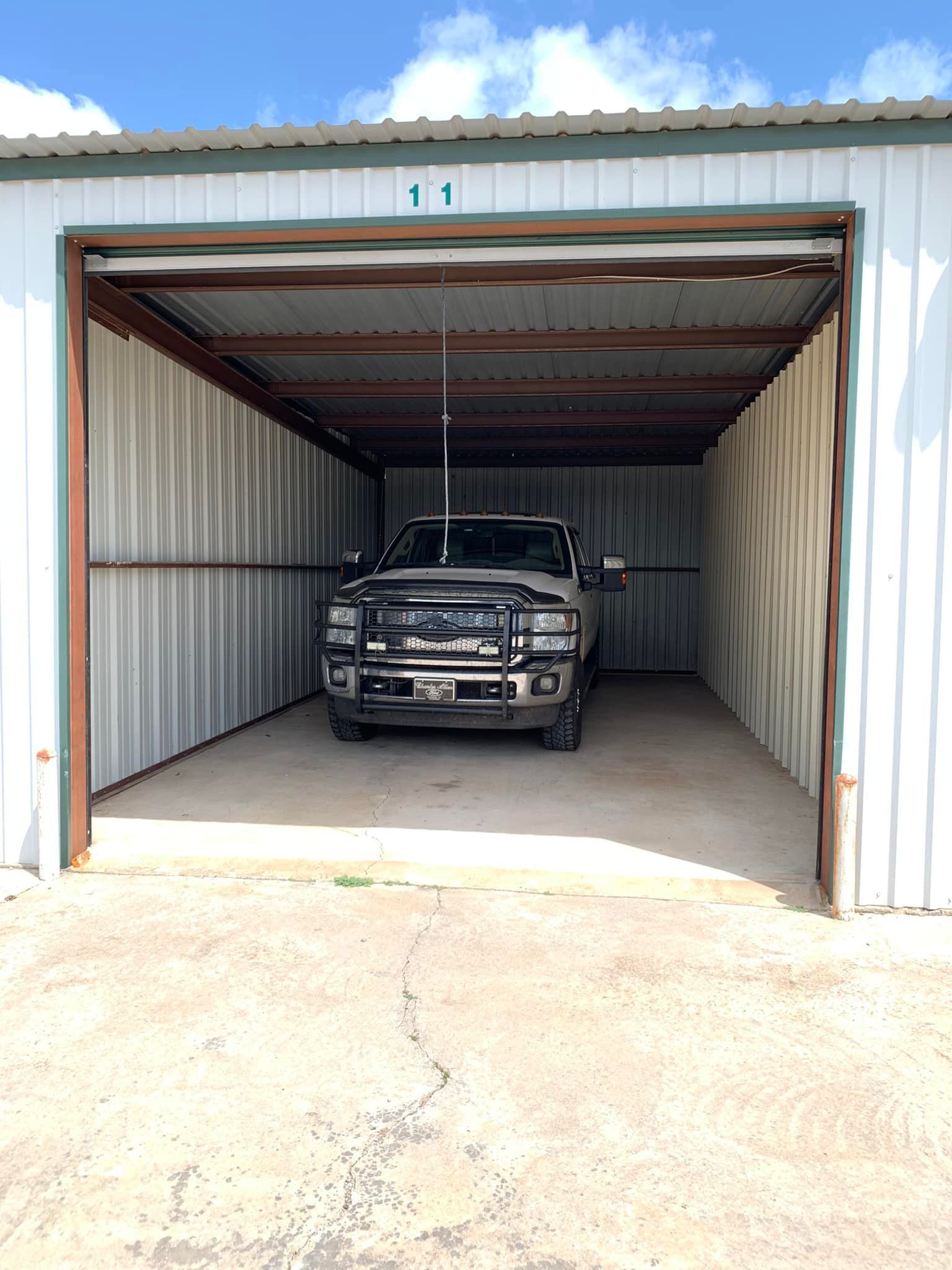 A black pickup truck parked inside a white metal storage unit under a blue, partly cloudy sky.