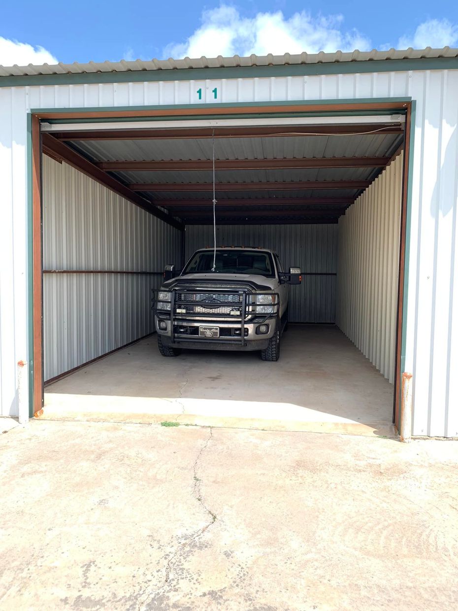 A black pickup truck parked inside a white metal storage unit under a blue, partly cloudy sky.