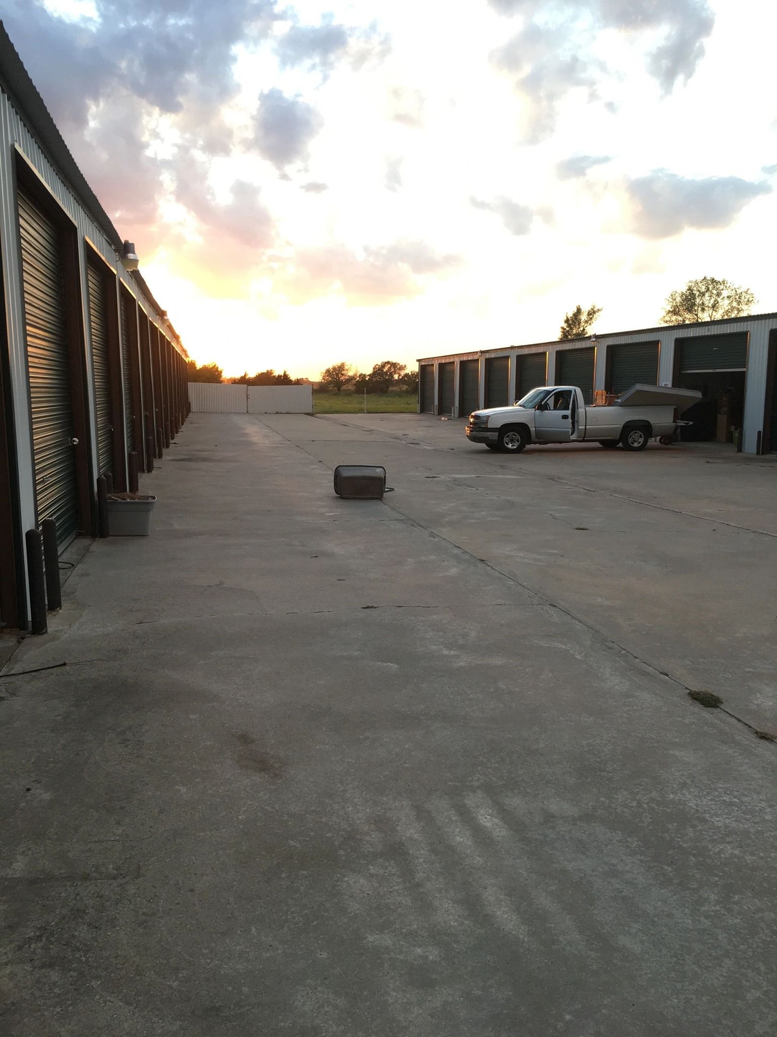 A sunset view of a long outdoor storage facility aisle with a white utility truck parked on the right.