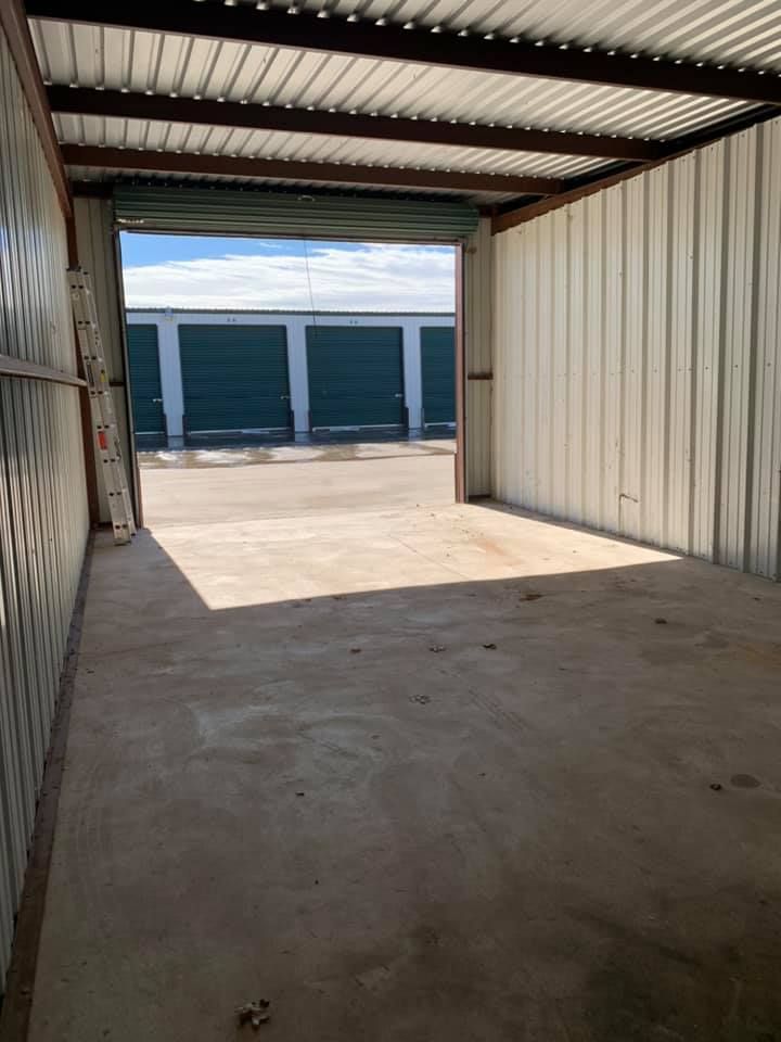 Interior view of an empty metal storage unit with the door open, facing a row of other storage units under a blue sky.
